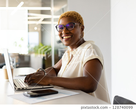 African American woman typing on laptop at desk in modern office with coffee cup, copy space African American woman typing on laptop at desk in modern office with coffee cup, copy space 128740099