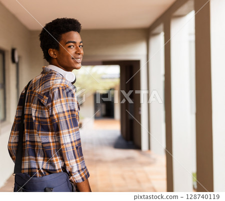 African American man glancing back in covered corridor with white headphones and navy bag African American man glancing back in covered corridor with white headphones and navy bag 128740119