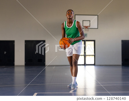 African American woman holding basketball, aiming shot on indoor basketball court with hoop, doors 128740140