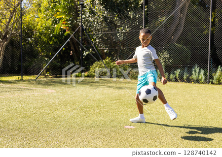 African American boy balancing soccer ball on artificial turf field with mesh fence, copy space African American boy balancing soccer ball on artificial turf field with mesh fence, copy space 128740142