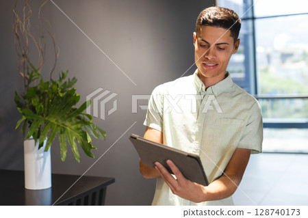 Man holding tablet and viewing screen in modern lobby with side table and plant, copy space 128740173