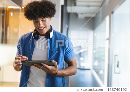 Man standing in modern office corridor using tablet and wearing headphones, copy space Man standing in modern office corridor using tablet and wearing headphones, copy space 128740192
