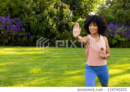 Woman practicing martial arts on lush garden lawn in sunny park, focusing on balance, copy space 128740201