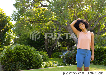Woman standing on manicured lawn in sunny garden, with green shrubs and wooden bench, copy space Woman standing on manicured lawn in sunny garden, with green shrubs and wooden bench, copy space 128740204