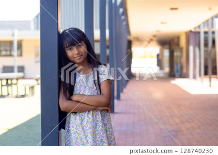 Girl child leaning on metal column in school hallway with brick walkway and columns, copy space 128740230