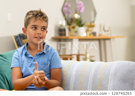 Male child giving thumbs up on patterned couch with green pillow in living room, copy space 128740265