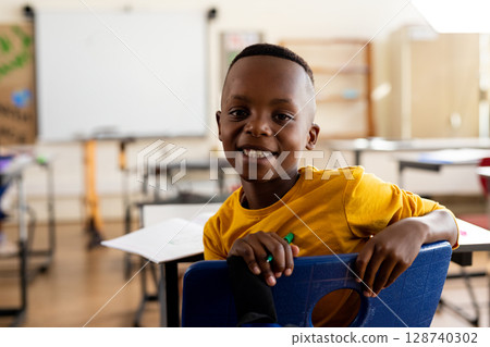 African American boy sitting backward on blue chair in classroom, holding green pencil, copy space African American boy sitting backward on blue chair in classroom, holding green pencil, copy space 128740302