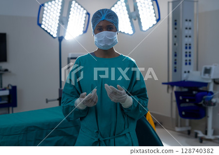 Young African American woman surgeon standing in operating room with surgical lights 128740382
