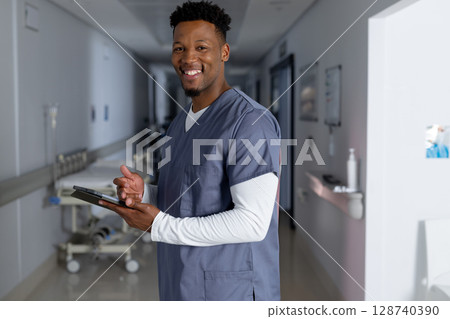 Young adult African American man standing in hospital corridor holding tablet near gurney 128740390
