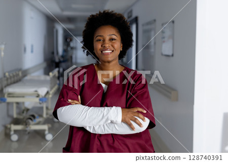 African American woman nurse smiling with crossed arms in hospital hallway, with gurney and boards African American woman nurse smiling with crossed arms in hospital hallway, with gurney and boards 128740391