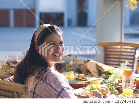 Woman turning and smiling toward camera at outdoor patio table, with roasted turkey and bread rolls 128740411