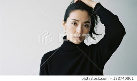 Portrait of a woman in a black turtleneck tucking her hair back 128740861