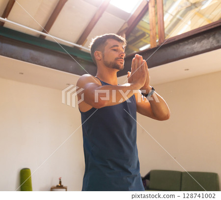 Young adult male practicing meditation in loft-style room with yoga mat and candle-lit side table Young adult male practicing meditation in loft-style room with yoga mat and candle-lit side table 128741002