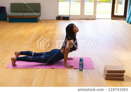 Woman practicing backbend on pink mat in yoga studio with blue water bottle and yoga blocks Woman practicing backbend on pink mat in yoga studio with blue water bottle and yoga blocks 128741003