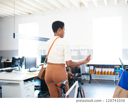 African American woman holding road bicycle with woven bag, pointing at window in modern office African American woman holding road bicycle with woven bag, pointing at window in modern office 128741038