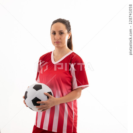 Young adult woman holding soccer ball in indoor studio, wearing red and white striped jersey 128741058