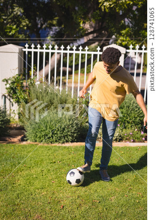 Man balancing black-and-white soccer ball on grassy lawn in residential yard, copy space 128741065