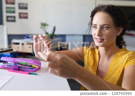 Female instructor examining small object at desk in classroom, with pink pencil case, copy space 128741093
