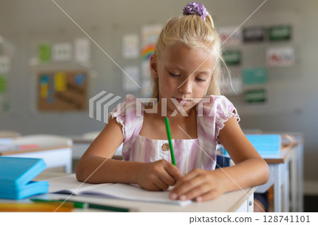 Girl around ten writing at desk in elementary classroom, using green colored pencil and notebook 128741101