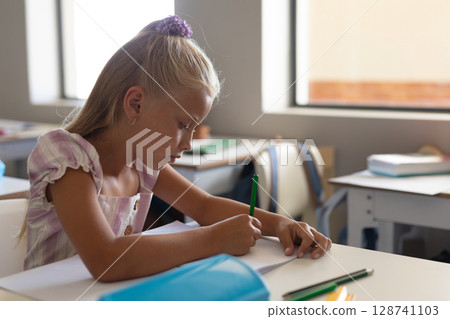 Schoolchild writing in bright classroom with green colored pencil and open notebook Schoolchild writing in bright classroom with green colored pencil and open notebook 128741103