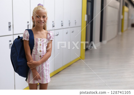 Schoolgirl standing in lit school hallway by white lockers, carrying navy backpack, copy space Schoolgirl standing in lit school hallway by white lockers, carrying navy backpack, copy space 128741105