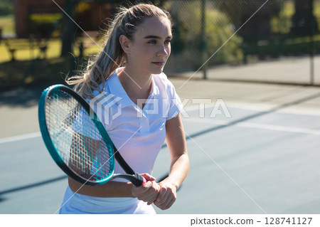 Young adult woman hitting backhand on outdoor tennis court, holding racket near chain-link fence 128741127