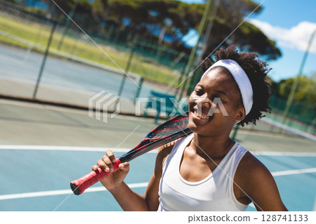 Woman standing on tennis court, resting racket over shoulder with headband and smile, copy space 128741133