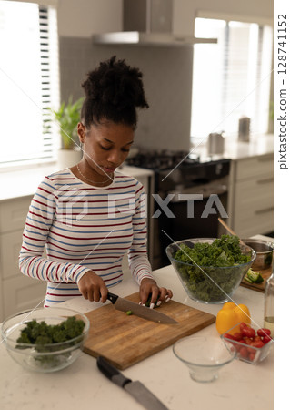 Woman chopping kale at kitchen island in home kitchen, with knife, bell pepper and cherry tomatoes Woman chopping kale at kitchen island in home kitchen, with knife, bell pepper and cherry tomatoes 128741152