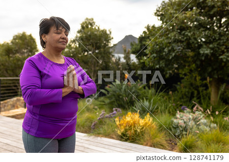 bi-racial senior woman practicing yoga on garden deck, with railing and succulents, copy space 128741179