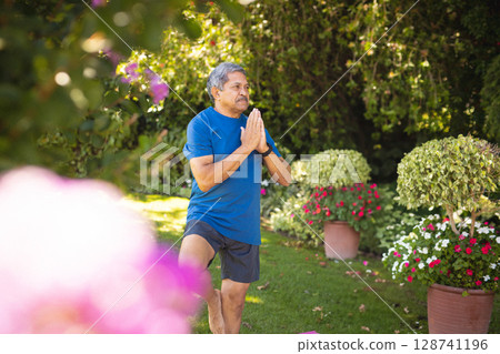Senior man practicing tree pose on pink mat in sunny backyard, with potted flowers, copy space Senior man practicing tree pose on pink mat in sunny backyard, with potted flowers, copy space 128741196