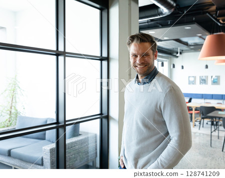 Mid adult man standing next to column in coworking lounge, with sofa, pendant lamps, copy space Mid adult man standing next to column in coworking lounge, with sofa, pendant lamps, copy space 128741209