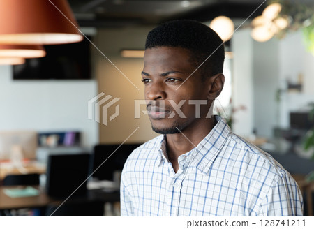 African American man standing in open-plan office, with computer monitors and desks, copy space 128741211
