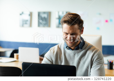 Man sitting at wooden desk in modern coworking space, working on black laptop with coffee cup Man sitting at wooden desk in modern coworking space, working on black laptop with coffee cup 128741220