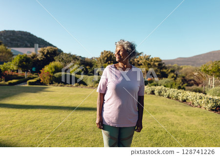 Senior woman standing and looking left in residential garden, enjoying sunshine and lush greenery 128741226