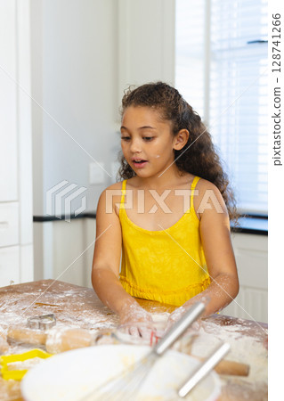 Girl mixing dough on flour-dusted kitchen countertop, with rolling pin cookie cutters and whisk 128741266