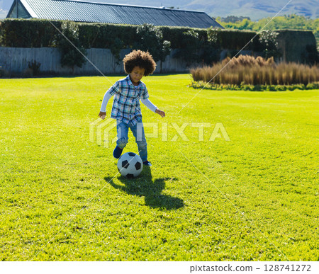 Young boy kicking black-and-white soccer ball in suburban backyard, bordered by fence and hedges Young boy kicking black-and-white soccer ball in suburban backyard, bordered by fence and hedges 128741272