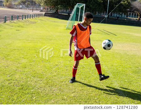 Male athlete juggling soccer ball on grass soccer pitch wearing red bib and cleats, copy space Male athlete juggling soccer ball on grass soccer pitch wearing red bib and cleats, copy space 128741280