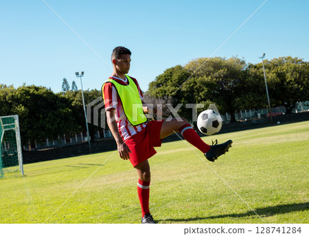 Male soccer player juggling soccer ball on soccer pitch, with fluorescent yellow bib, copy space Male soccer player juggling soccer ball on soccer pitch, with fluorescent yellow bib, copy space 128741284