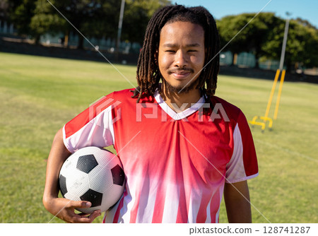 Man wearing red and white jersey holding soccer ball on grass training field with yellow hurdles Man wearing red and white jersey holding soccer ball on grass training field with yellow hurdles 128741287