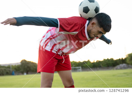 Male soccer player balancing black-and-white ball on back at grassy pitch, showing balance skill 128741296