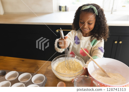 African American girl whisking batter in home kitchen, with glass bowl and muffin tin, copy space African American girl whisking batter in home kitchen, with glass bowl and muffin tin, copy space 128741313
