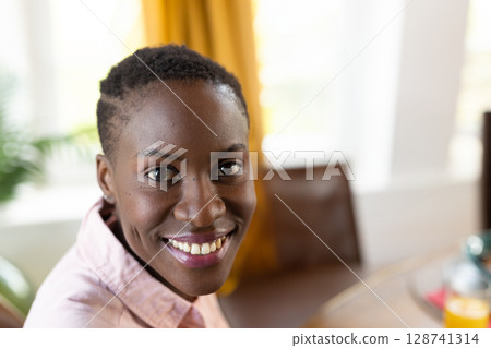 Mid?adult African American woman smiling in indoor dining area, with wooden table and orange juice 128741314