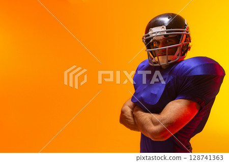 Male football player standing arms crossed in studio, with helmet and shoulder pads, copy space Male football player standing arms crossed in studio, with helmet and shoulder pads, copy space 128741363
