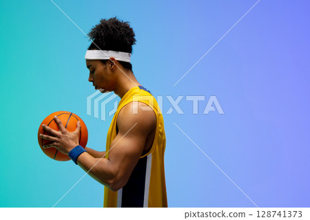 Male basketball player holding orange ball in studio wearing yellow jersey and headband, copy space 128741373