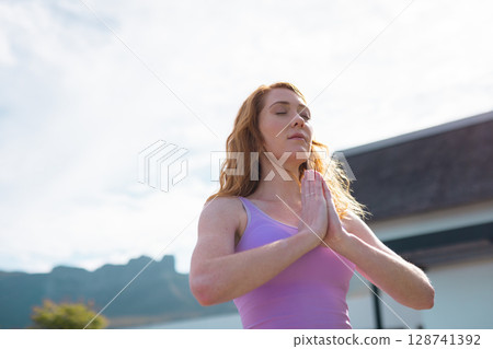 Woman practicing meditation on balcony overlooking mountain landscape, wearing lilac tank top 128741392