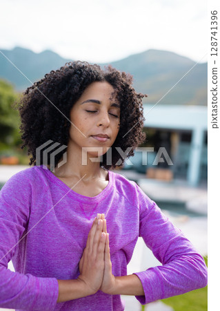 Mid adult woman practicing yoga on poolside patio outside modern house, overlooking mountains Mid adult woman practicing yoga on poolside patio outside modern house, overlooking mountains 128741396