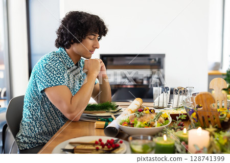 Young man sitting at wooden dining table at home, with salad bowl and candles, copy space 128741399
