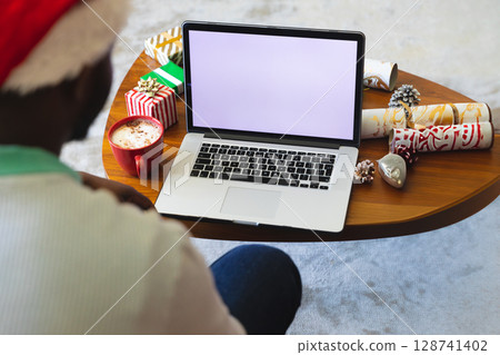 African American man using laptop at home with coffee mug, gifts, Christmas crackers and pine cones African American man using laptop at home with coffee mug, gifts, Christmas crackers and pine cones 128741402