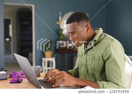 African American man typing on laptop at home office desk with purple hole punches, copy space 128741409