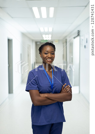 African American nurse standing in hospital hallway, holding blue lanyard ID badge and smiling African American nurse standing in hospital hallway, holding blue lanyard ID badge and smiling 128741431